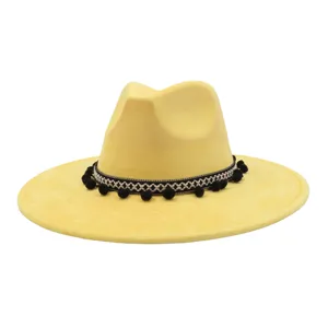 Yellow soft suede fedora hat with ethnic woven band and black pom poms, detail view.