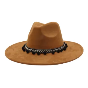 Detailed view of brown suede fedora hat featuring black white embroidered band and pom-poms.
