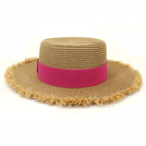 Nahansicht eines stilvollen Strohhutes mit flacher Krone, rosa Band und Fransenrand.