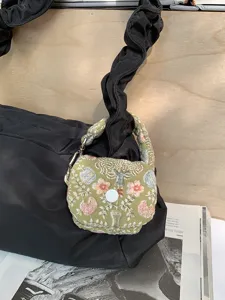 Detailed view of black puffy shoulder bag with cute green embroidered mini pouch charm.