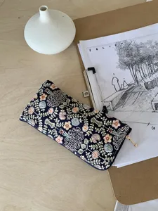 Close-up detail of a dark blue floral embroidered glasses storage pouch with gold zipper pull.