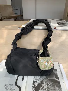 Detailed view of black puffy shoulder bag featuring a green floral embroidered mini pouch accessory.