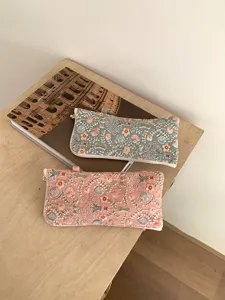 Detailed view of embroidered glasses pouch case, exquisite floral pattern, zipper closure, table.