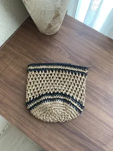 Detalle de bolso tejido a mano, patron de malla hueca, bolsa cosmetica de paja negra y marron.