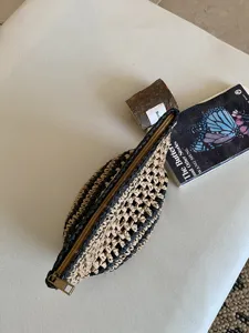 Vista de cerca de una bolsa cosmética de paja tejida negra y natural con una cremallera dorada.