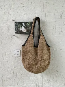 Vue détaillée d'un sac porté épaule en paille tissée accroché sur un mur texturé.