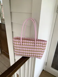 Detailansicht der rosa-braunen geflochtenen Tasche auf einem Holzgeländer im Verandabereich.