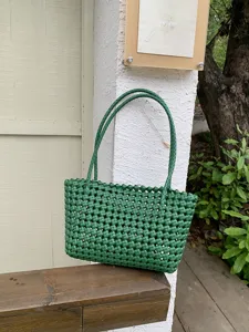Green woven hollow beach bag detail, showing fine texture and dual handles for summer.