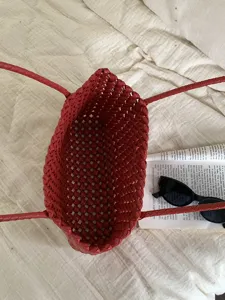 Red woven plastic beach tote bag detail showing intricate grid pattern and dual handles.