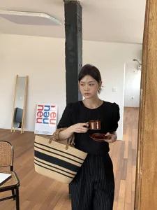 Dettaglio borsa shopper in paglia a righe fatta a mano, con manici in bambù e capienza.
