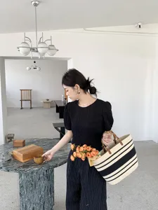 Vista in ambientazione di una borsa a mano intrecciata a righe con manici di bambù chic.