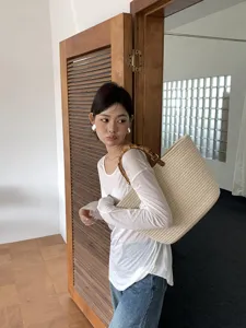 Vista dettagliata di una borsa tote intrecciata beige con manici in bambù al chiuso.