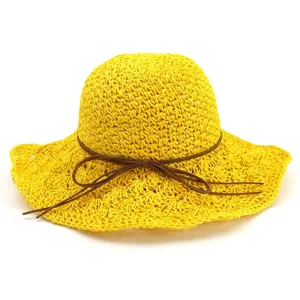 Detailed view of the handmade yellow straw sun hat featuring a chic brown leather cord bow.