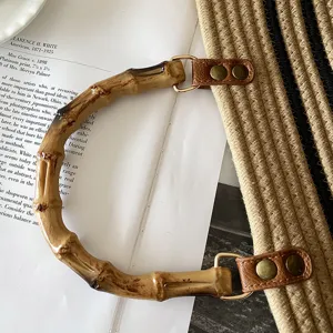 Dettaglio di una borsa in paglia intrecciata con manico curvo in bambù e linguette in pelle.