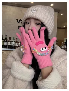 Cute quirky pink knit gloves detail view, funny plush eyes and braided hair design, warm winter.
