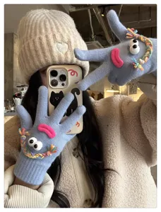 Close-up detail of quirky blue knitted gloves featuring funny googly eyes and pink lips.