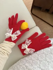 Close-up detail of women's winter cute red knit gloves with white lace and bow decor.