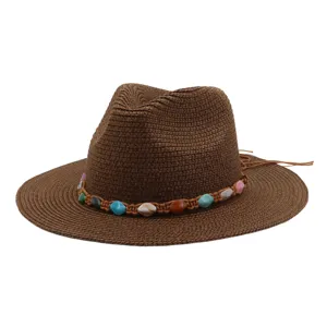 Gros plan sur un chapeau de paille marron avec une bande tressée de perles et des pompons.