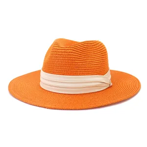 Detailed close-up of this vibrant orange straw fedora hat, featuring a stylish beige ribbon.