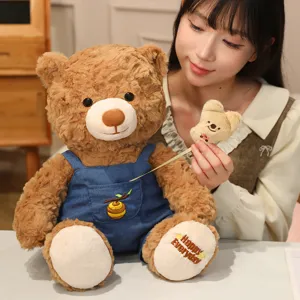 Cute plush teddy bear toy with blue denim overalls and honey pot embroidery, soft huggable.