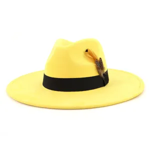 Close-up detail of yellow suede fedora hat featuring black ribbon and decorative feather.
