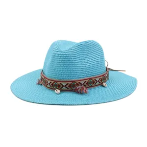 Close-up detail of the woven blue straw sun hat featuring ethnic pattern ribbon, tassels, and shell decor.
