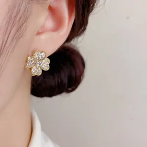 Pendientes de tuerca con trébol de cuatro hojas de circón dorado, detalle brillante de cerca.