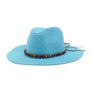 Gros plan de détail du chapeau de paille bleu clair avec perles colorées et lanière.