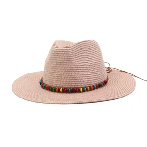 Détail de chapeau de paille rose avec bande de perles colorées et texture tissée estivale.
