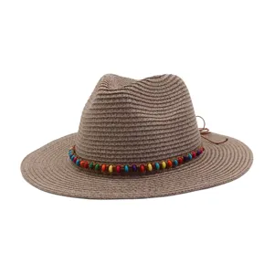 Gros plan du chapeau de paille marron mettant en valeur le bandeau de perles et la texture.