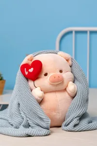 Cute plush pig toy detail showing soft pink fabric holding a red heart balloon in cozy blanket.
