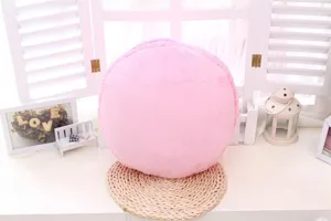 Detailaufnahme des weichen rosa runden Plüsch-Macaron-Kissens auf einer geflochtenen Matte.