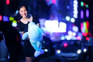 Vista dettagliata del simpatico peluche di delfino blu luminoso tenuto da una modella di notte.