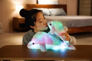 Dettaglio peluche delfino luminoso, ambiente camera da letto accogliente con luci LED colorate.