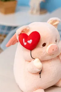 Cute angel pig plush toy detail showing soft pink fabric, wings, and red heart balloon.