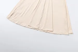 Close-up detail of women's pleated skirt hem in solid light beige color, soft fabric texture.