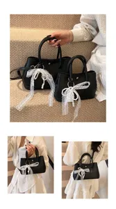 Detailansicht der schwarzen Damen Handtasche mit weißer Spitzen Schleife und Perlenanhänger.