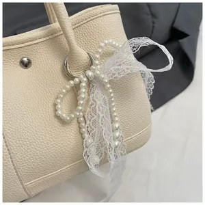 Detailansicht einer stilvollen beigen Handtasche mit weißer Spitzen-Perlen-Schleife.