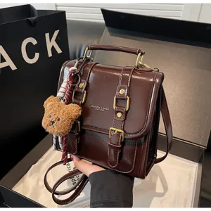 Dettaglio zainetto in pelle marrone, borsa elegante con simpatico ciondolo orsetto e fibbie in metallo.
