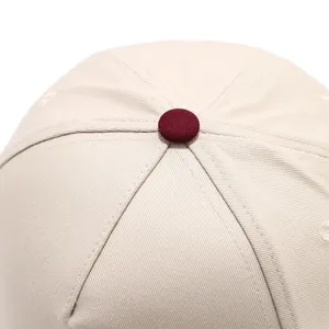 Close-up detail of khaki baseball cap top, featuring neat stitching and a contrast maroon button.