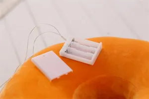 Detailed close-up view of soft plush donut pillow featuring battery compartment and wires.