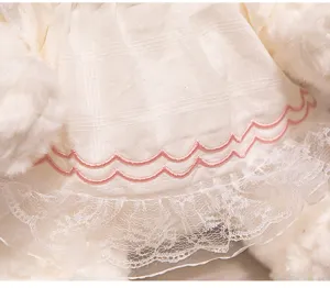 Detalle vestido muñeca de peluche, tela de cuadros beige con bordado rosa y encaje blanco.