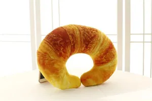Primer plano de almohada cervical de felpa con forma de cruasán y detalle de impresión 3D realista.