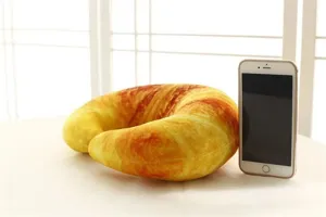 Almohada cervical de felpa suave en forma de U con diseño de cruasán realista.