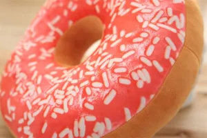 Close-up detail of the soft plush donut pillow showing pink frosting and sprinkles texture.