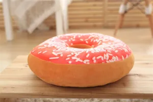 Detailed close-up of soft plush donut cushion featuring pink frosting and white sprinkles.
