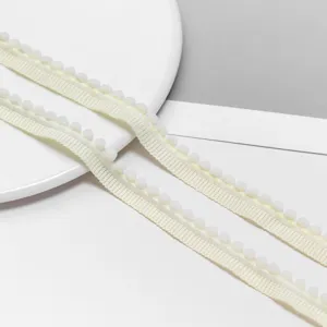 Close-up detail of cream pom-pom trim ribbon, ideal for DIY doll clothes and gift wrapping.