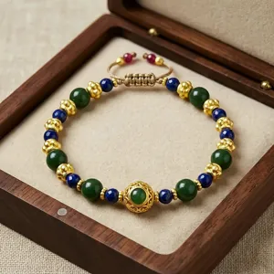 Detail des Perlenarmbands mit grünen und blauen Steinen sowie goldenen Abstandshaltern in Holzkiste.