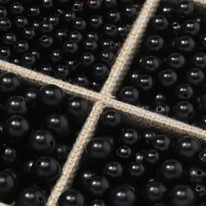Close-up detail of smooth black wood loose beads arranged in partitioned storage grid.
