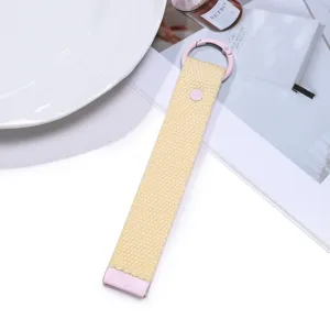 Yellow woven strap keychain with pink metal hardware, minimalist bag pendant detail view.